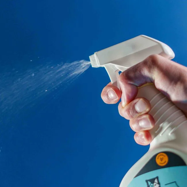 A man cleaning a glass door indoors using a spray bottle and cloth.
